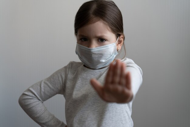 Detener el concepto de brote de coronavirus o covid 19 - niña con máscara protectora médica muestra un gesto de parada con la mano - niña tendida con la palma de la mano con miedo, concepto de cuarentena o aislamiento en el hogar
