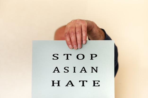 Detener el concepto de odio asiático. Mano de hombres sosteniendo una hoja de papel de tarjeta con la palabra detener el odio asiático para el cartel de la campaña