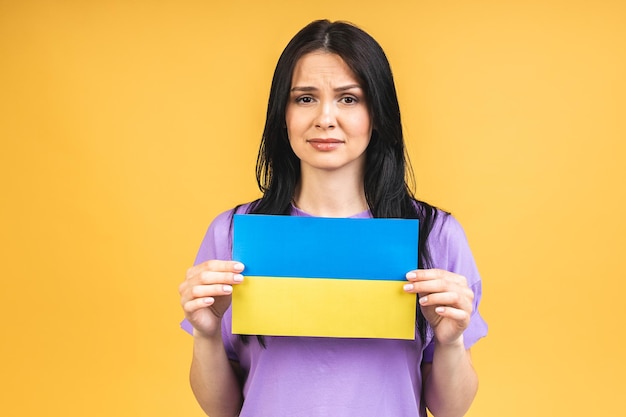 Detener la guerra en Ucrania Retrato de mujer enojada agresiva triste sosteniendo en las manos la bandera ucraniana aislada sobre fondo amarillo