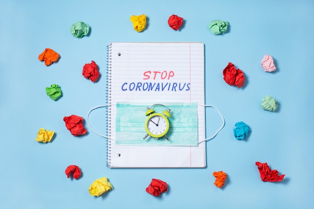 Detener el texto del coronavirus escrito en un cuaderno abierto y un reloj despertador