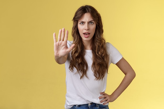 Detente ahí mismo, policía de la moda. Chica joven de pelo rizado confiada de aspecto serio tirar de la mano suficiente gesto de prohibición demanda situación final prohibir amigo conducir soporte fondo amarillo