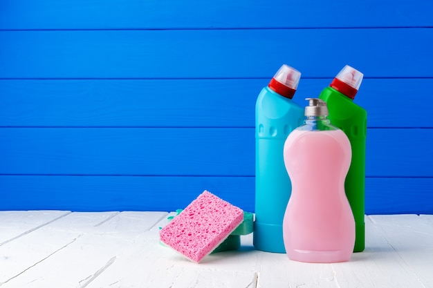 Detergente de limpeza e esponjas na mesa contra um fundo azul