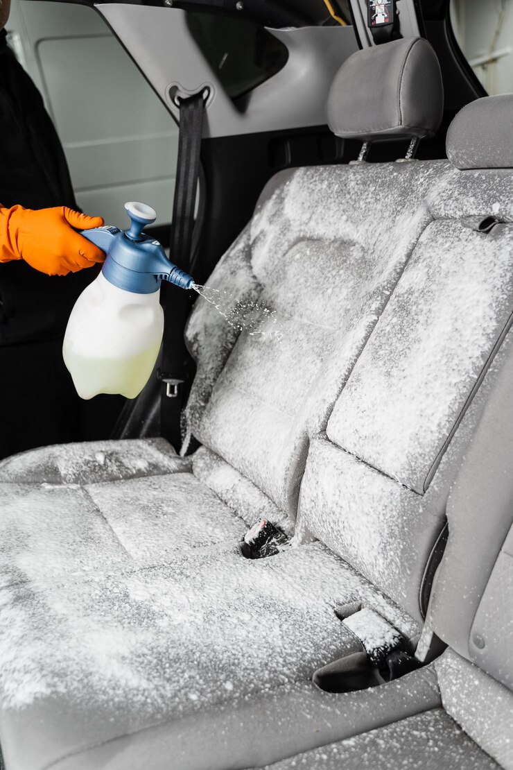 Foto detergente de pulverização em assentos têxteis no interior do carro para limpeza a seco limpador profissional em luvas está derramando detergente no assento do carro para remover manchas e sujeira