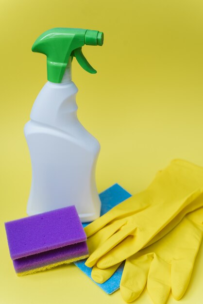 Detergente, esponja e luvas para limpar a casa em um fundo amarelo brilhante