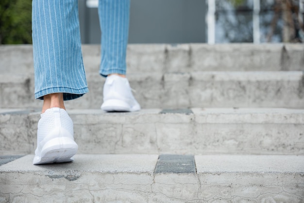 Con determinación, una mujer con zapatillas de deporte sube las escaleras de la ciudad reflejando su implacable progreso cada paso simboliza su compromiso con el éxito y el crecimiento continuo.