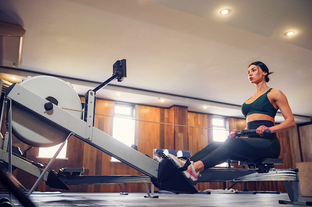 Determinada joven trabajando en la máquina de la fila en el gimnasio