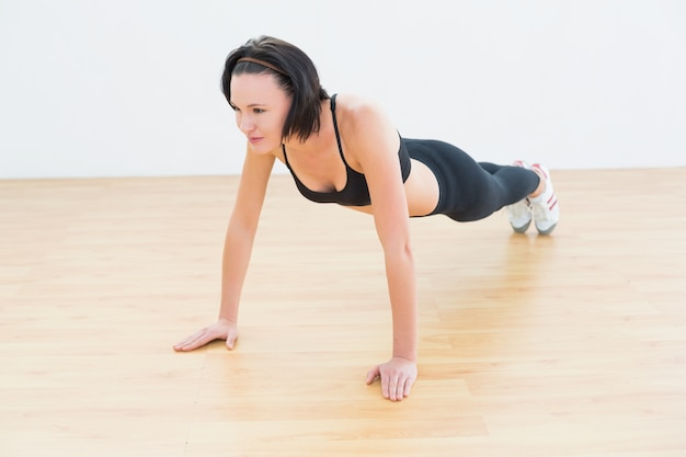 Determinada mujer deportiva haciendo flexiones en gimnasio