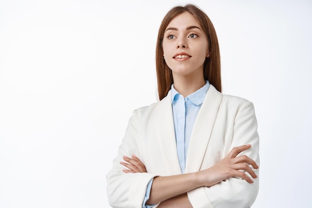 Determinada mujer directora ejecutiva de oficina profesional que usa traje de negocios cruza los brazos en el pecho mira a un lado con cara esperanzada y segura de fondo blanco