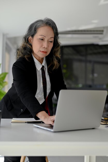 Determinada mujer de negocios de edad asiática que usa una computadora portátil que trabaja en la oficina