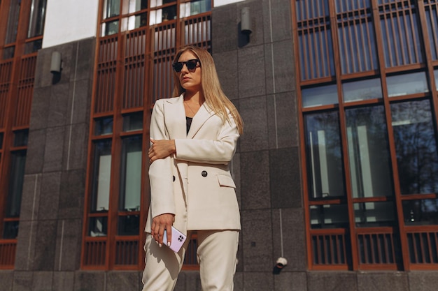 determinada mujer de negocios con smartphone y elegante traje blanco