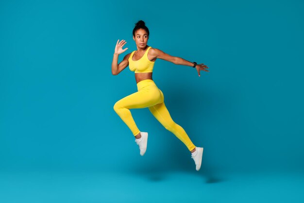 Determinada mulher de fitness afro-americana salta contra o fundo azul do estúdio