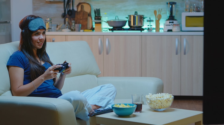 Foto determinada mulher jogando videogame na sala de estar à noite. mulher empolgada gamer sentada no sofá, jogando e ganhando videogames usando o console e o controlador sem fio.
