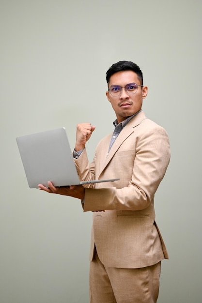 Determinado hombre de negocios asiático con una computadora portátil que muestra el puño cerrado de pie contra el fondo verde