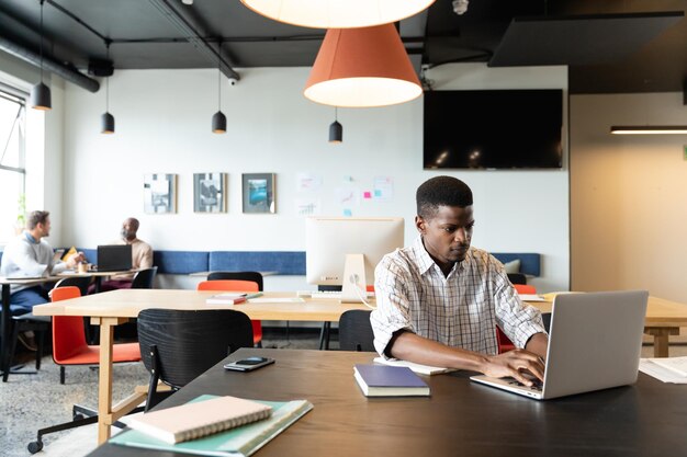 Foto determinado jovem empresário afro-americano trabalhando em laptop no escritório criativo