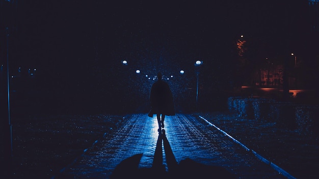 Detetive masculino em um chapéu e capa de chuva à noite em uma cidade chuvosa