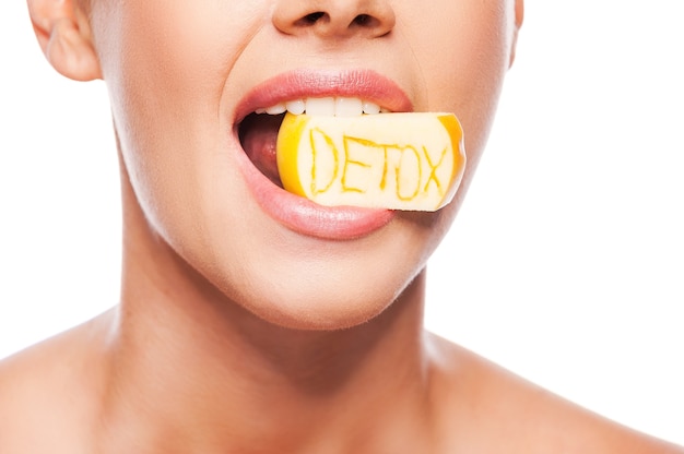 Detox-Diät. Nahaufnahme einer schönen jungen Frau mit nacktem Oberkörper, die ein Stück Apfel im Mund mit Detox-Text hält, während sie vor weißem Hintergrund steht