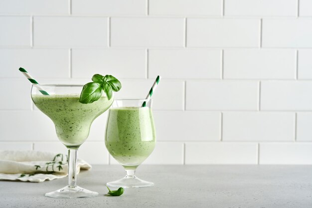 Detox jugo de vegetales verdes o batido adornado con hojas de albahaca fresca en copa de cóctel sobre fondo gris claro de pizarra, piedra u hormigón. Vista superior con espacio de copia.