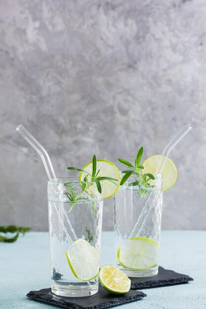 Detox-Trinkwasser mit Limette und Rosmarin in Gläsern mit Öko-Strohhalm auf dem Tisch Vertikale Ansicht