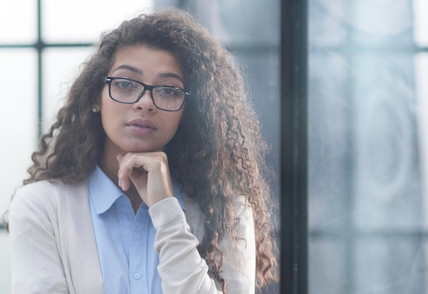 Desde detrás del cristal, una joven mujer de negocios mirando por la ventana de la oficina