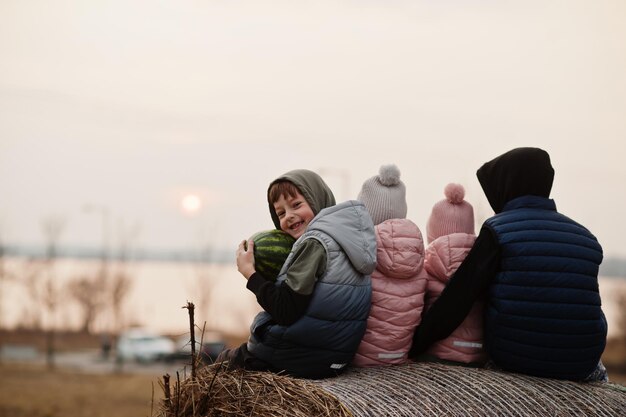 Detrás de cuatro niños sentados en un pajar en el campo contra el atardecer del lago