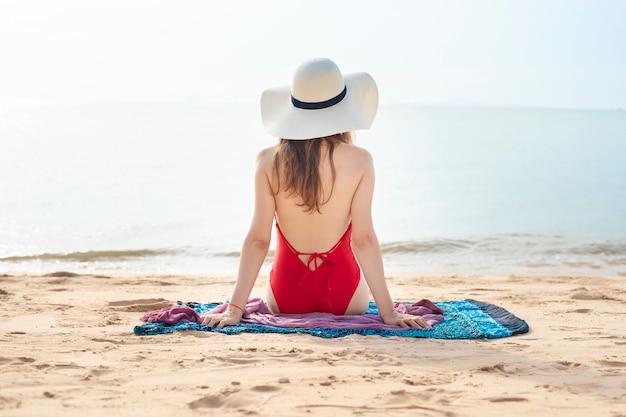 Detrás de hermosa mujer en traje de baño rojo está sentado en la playa