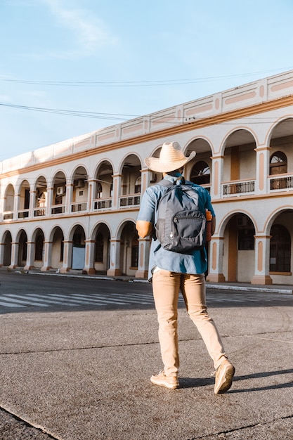 Foto detrás del hombre viajero con mochila y sombrero caminando por una calle en la ceiba atlantida honduras