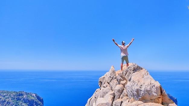 Detrás de inspirado despreocupado alegre feliz solo tipo viajero se encuentra con los brazos abiertos en la cima de un acantilado Motivación y éxito