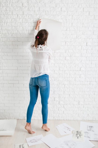 Detrás de la mujer colgando papel vacío en la pared