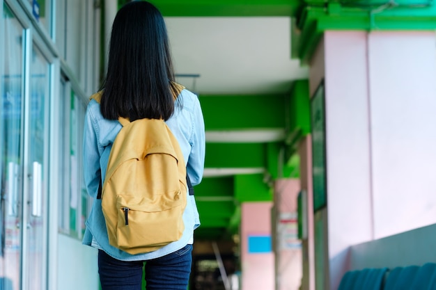 Detrás de la niña estudiante que sostiene los libros y lleva la mochila mientras camina en el campus