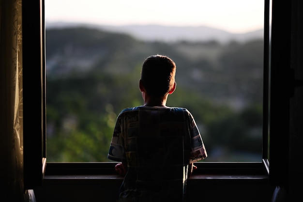 Detrás del niño mirando desde la ventana al atardecer