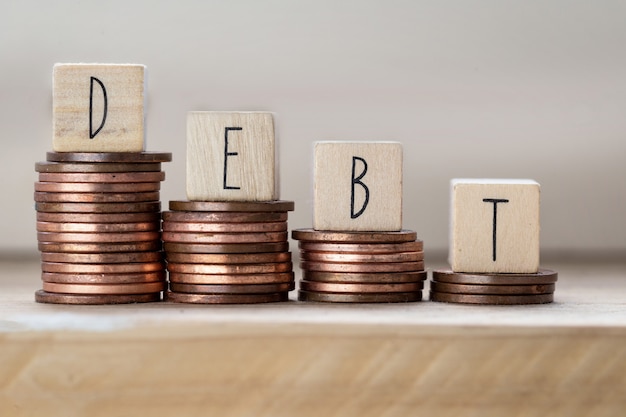 Deuda escrita en cubos de madera con letras, montones de monedas