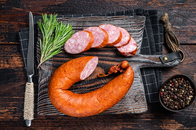 Deutsche geräucherte Wurst auf einem rustikalen Holzbrett mit Thymian. Dunkler hölzerner Hintergrund. Ansicht von oben.