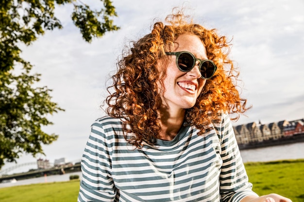Deutschland, Köln, Porträt einer lachenden rothaarigen jungen Frau mit Sonnenbrille