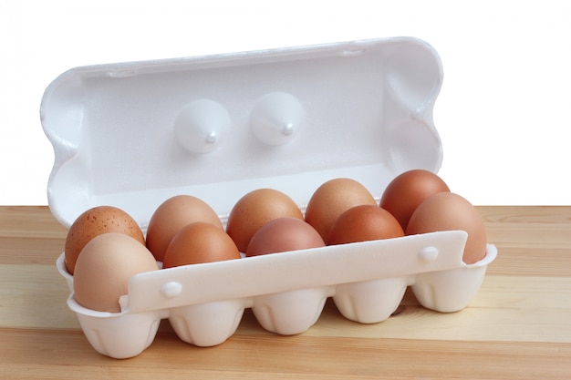 Dez ovos marrons da galinha na embalagem branca em uma tabela de madeira, isolado.