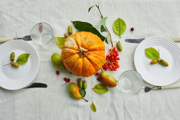 El día de acción de gracias o el ajuste de lugar de la mesa de la cena de Halloween decorativo con calabaza, bellotas, hojas de peras sobre fondo de mantel blanco, vista desde arriba, vista superior, endecha plana.