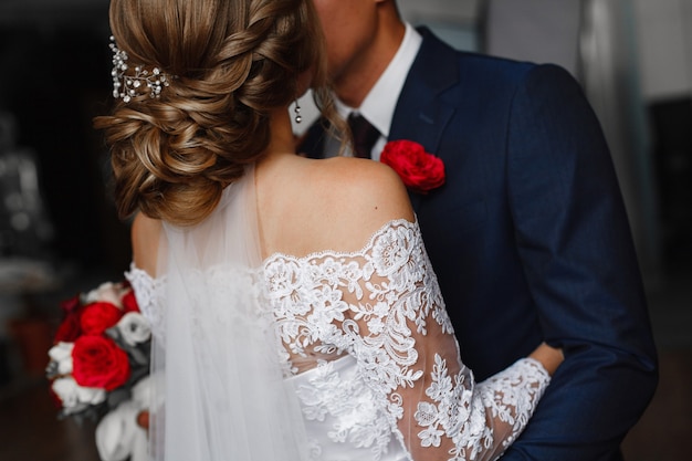 día de la boda. Recién casados besándose en la ceremonia de matrimonio. abrazos apasionados de una pareja amorosa. Novio con ojal abrazando suavemente a la novia con ramo rojo. Momento romántico de boda.