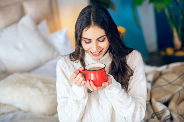 Dia bom. Mulher de cabelos escuros com uma xícara vermelha nas mãos, parecendo relaxada