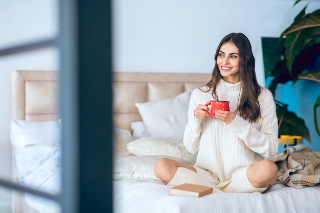 Dia bom. Mulher de cabelos escuros com uma xícara vermelha nas mãos, parecendo relaxada