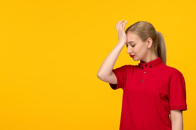 Día de la camisa roja chica confundida tocando su frente en una camisa roja sobre un fondo amarillo