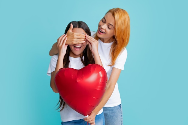 Día de cumpleaños Sonriente madre e hija sosteniendo globo de corazón de amor sobre fondo azul Feliz