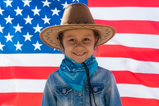 Dia da Independência. Feriado patriótico. Criança feliz, menina criança bonitinha com bandeira americana. Vaqueiro. EUA celebram 4 de julho.