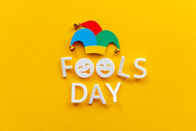Dia da mentira sobre fundo amarelo com chapéu de bobo Cartão de primeiro abril com emojis de rosto feliz