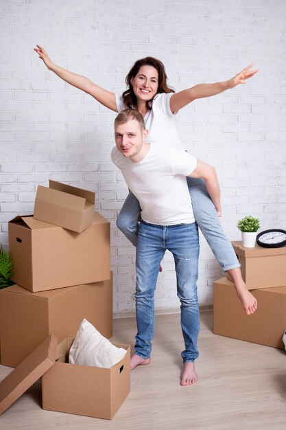Dia da mudança - jovem casal feliz se divertindo em sua nova casa ou apartamento cercado de caixas de papelão