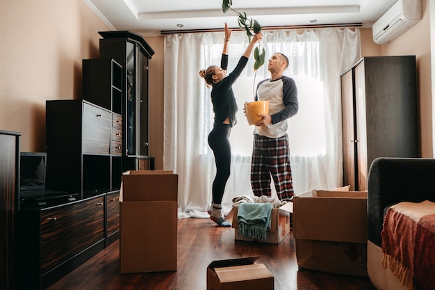 Dia da mudança mudando para nova casa jovem casal feliz família de recém-casados se divertindo no quarto com a planta de casa