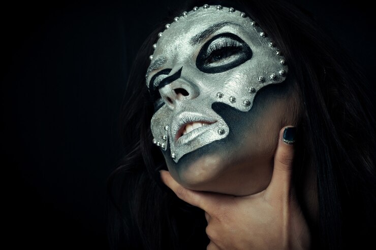 Foto dia das bruxas, feriados, estilo de vida, pessoas, beleza, conceito criativo - tema de halloween e maquiagem criativa: modelo de menina bonita com corpo preto com máscara prateada pintura do crânio em fundo escuro no estúdio