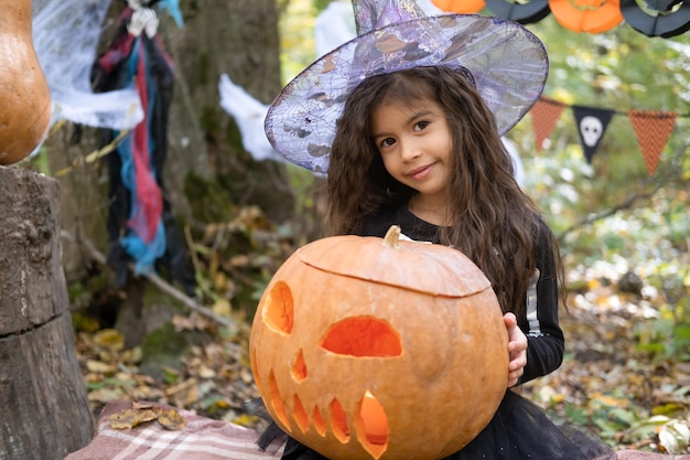 Dia das Bruxas. linda garota árabe fantasiada de bruxa com abóbora ao ar livre, se divertindo, comemorando o Halloween