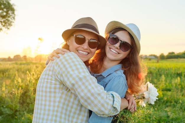 Dia das mães, abraçando a filha adolescente feliz e sorridente com a mãe no prado com buquê de flores