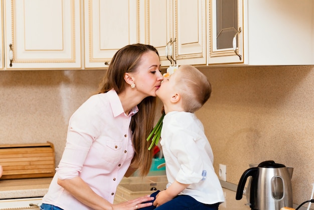 Dia das mães, feriados e conceito de família - filho pequeno feliz dá flores para sua mãe sorridente em casa. Uma criança dá à mãe um buquê de narcisos