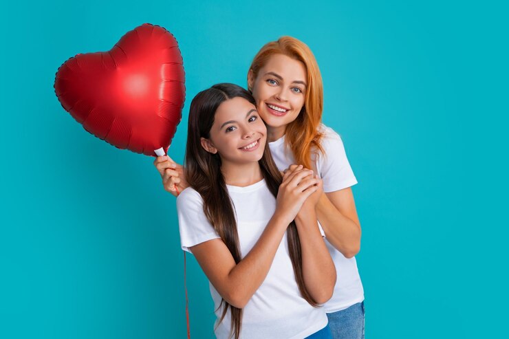 Foto dia de aniversário mãe e filha sorridentes segurando balão de coração de amor em fundo azul feliz