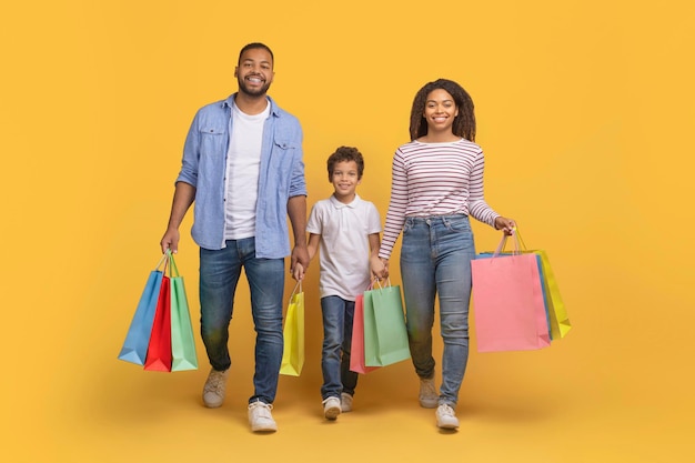 Dia de compras uma alegre família afro-americana de três pessoas a caminhar com sacos de compras